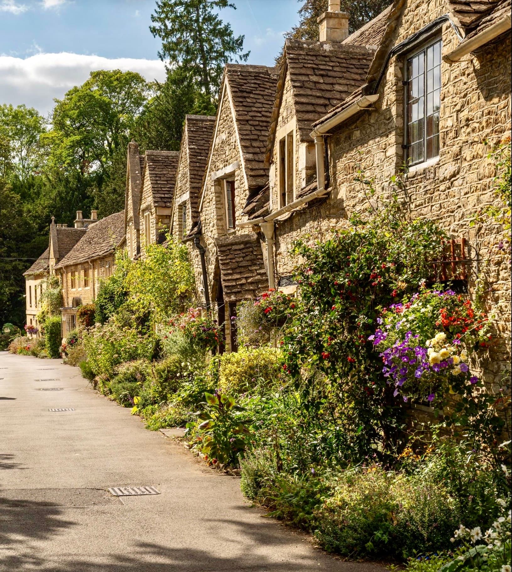 Historic stone cottages with gabled roofs and colorful flower gardens along a village street.